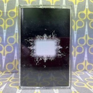 May include: A black cassette tape with a white, abstract design on the front. The design is a white square with a jagged, spiky border.