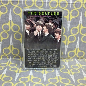 K&ouml;nnte beinhalten: Eine Kassette mit einem Foto der Beatles auf der Vorderseite. Der Titel "THE BEATLES" ist in Wei&szlig; auf schwarzem Hintergrund gedruckt. Die Kassette ist mit "Rock 'n' Roll Music Volume 1" beschriftet und listet die auf der Kassette enthaltenen Songs auf: "Rock and Roll Music", "Slow Down", "Kansas City", "Hey, Hey, Hey, Hey", "Money (That's What I Want)", "Bad Boy", "Matchbox", "Roll Over Beethoven", "Twist and Shout", "I Saw Her Standing There", "You Can't Do That", "I Wanna Be Your Man", "I Call Your Name", "Boys", "Long Tall Sally".
