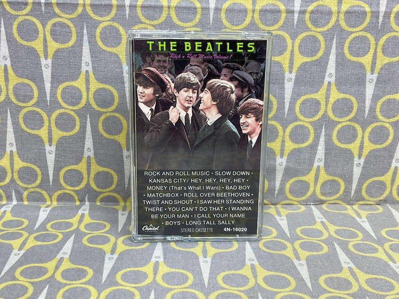 K&ouml;nnte beinhalten: Eine Kassette mit einem Foto der Beatles auf der Vorderseite. Der Titel "THE BEATLES" ist in Wei&szlig; auf schwarzem Hintergrund gedruckt. Die Kassette ist mit "Rock 'n' Roll Music Volume 1" beschriftet und listet die auf der Kassette enthaltenen Songs auf: "Rock and Roll Music", "Slow Down", "Kansas City", "Hey, Hey, Hey, Hey", "Money (That's What I Want)", "Bad Boy", "Matchbox", "Roll Over Beethoven", "Twist and Shout", "I Saw Her Standing There", "You Can't Do That", "I Wanna Be Your Man", "I Call Your Name", "Boys", "Long Tall Sally".