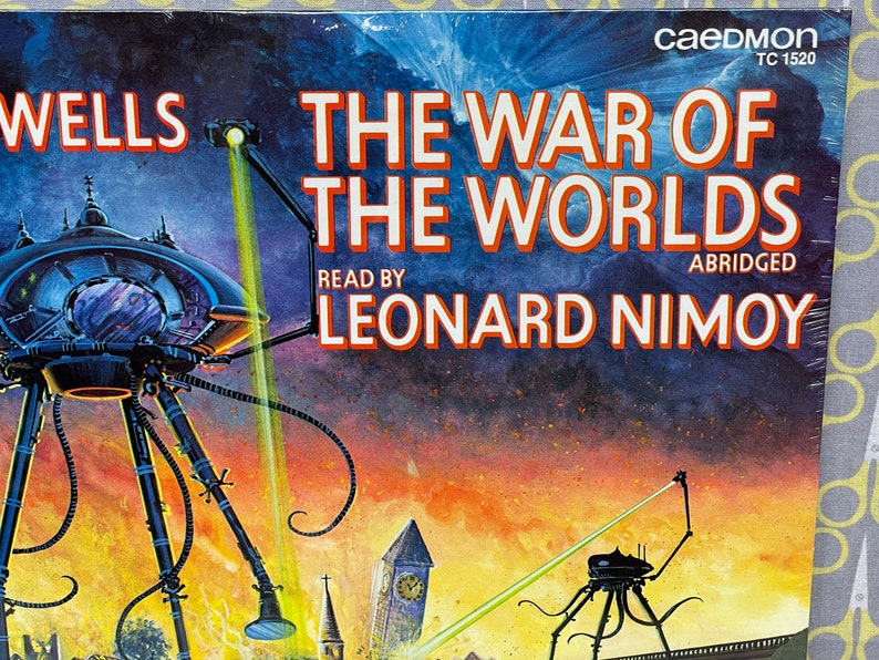 May include: A vintage audio cassette tape cover featuring an illustration of a Martian tripod from the book "The War of the Worlds" by H.G. Wells. The cover is blue and orange with the title "The War of the Worlds" in white text. The text "Read by Leonard Nimoy" and "Abridged" are also visible on the cover.