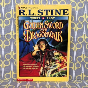May include: A yellow and red book cover with the title "Golden Sword of Dragonwalk" by R.L. Stine. The cover features a man in a red and black robe with a green and yellow magical effect around his hand. The book is part of the "Twist a Plot" series.