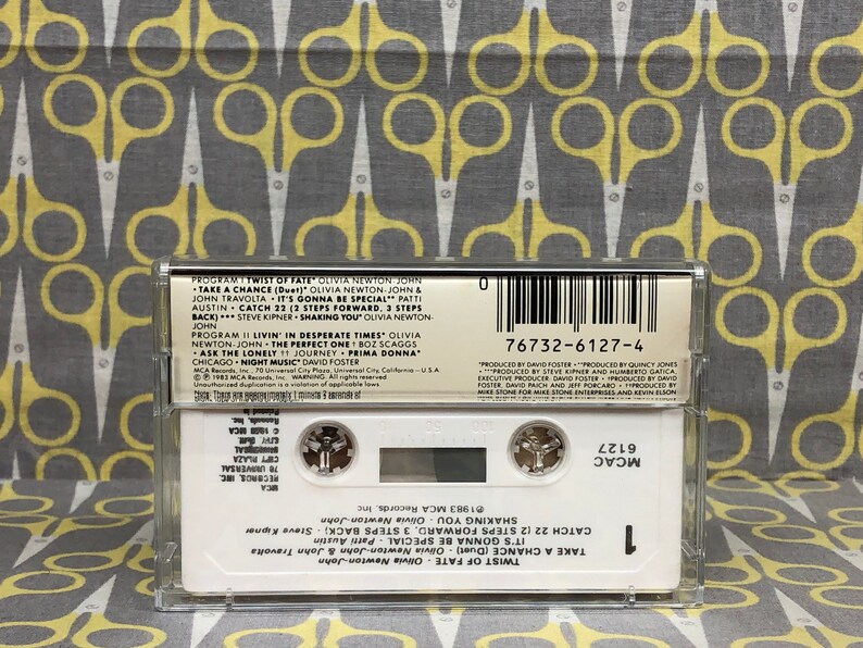 May include: A white cassette tape with a clear plastic case. The tape is labeled "Twist of Fate" by Olivia Newton-John. The track list includes "Take a Chance", "It's Gonna Be Special", "Catch 22", "Shaking You", and "Livin' in Desperate Times".