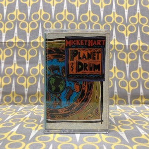 May include: A cassette tape with a colorful illustration of a globe and the text "Mickey Hart Planet Drum" on the front.
