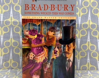 Può includere: Un libro tascabile intitolato Something Wicked This Way Comes di Bradbury, con un'illustrazione di copertina che mostra una persona su un cavallo da giostra viola accanto a un uomo con cilindro nero e abito su un cielo scuro e tempestoso.