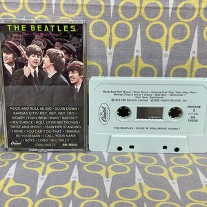 K&ouml;nnte beinhalten: Ein wei&szlig;es Kassettenband mit einem Bild der Beatles auf der Vorderseite. Das Band ist mit "The Beatles Rock 'n' Roll Music Volume 1" beschriftet und enth&auml;lt auf der R&uuml;ckseite eine Liste der Songs. Das Band ist eine Ver&ouml;ffentlichung von Capitol Records.