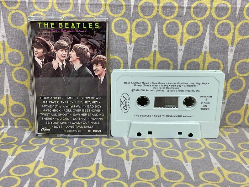 K&ouml;nnte beinhalten: Ein wei&szlig;es Kassettenband mit einem Bild der Beatles auf der Vorderseite. Das Band ist mit "The Beatles Rock 'n' Roll Music Volume 1" beschriftet und enth&auml;lt auf der R&uuml;ckseite eine Liste der Songs. Das Band ist eine Ver&ouml;ffentlichung von Capitol Records.