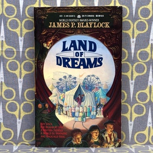 May include: A book cover featuring a colourful illustration of a carnival with a Ferris wheel, tents, and people. The title of the book is "Land of Dreams" by James P. Blaylock. The book cover is against a grey and yellow patterned background.