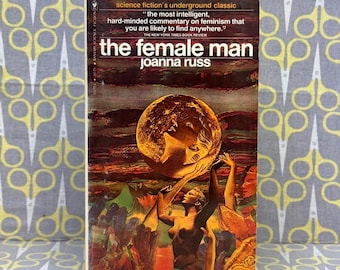 May include: A vintage paperback book titled "the female man" by Joanna Russ. The cover features a surreal illustration with a large, glowing orb and figures reaching upwards. The book is a science fiction classic.
