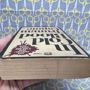 May include: A close-up of the spine of a paperback book titled "In Cold Blood" by Truman Capote. The book is worn and has a brown cover with black text. The text on the spine indicates that this is the 19th printing and over 3,100,000 copies have been sold.
