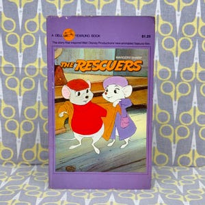 May include: A purple paperback book with the title "The Rescuers" in white lettering. The book cover features two cartoon mice, one wearing a red hat and the other wearing a purple hat. The book is a Dell Yearling Book and the text "The story that inspired Walt Disney Productions new animated feature film" is printed on the cover.