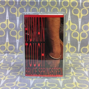 May include: A cassette tape with a red and white label. The label says "Human Touch" and "Bruce Springsteen".