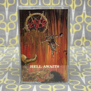 May include: A cassette tape with the album art for Slayer's "Hell Awaits." The artwork features a hellish scene with a red and orange background, a demonic figure, and the band's logo in red. The text "HELL AWAITS" is visible.