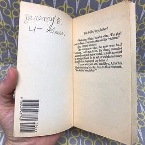 May include: A close-up of a book's back cover with a barcode and the text "You killed my father!"  The book is open to a page with text about a creature that is half human and half machine. The text also includes the name "Ryu".