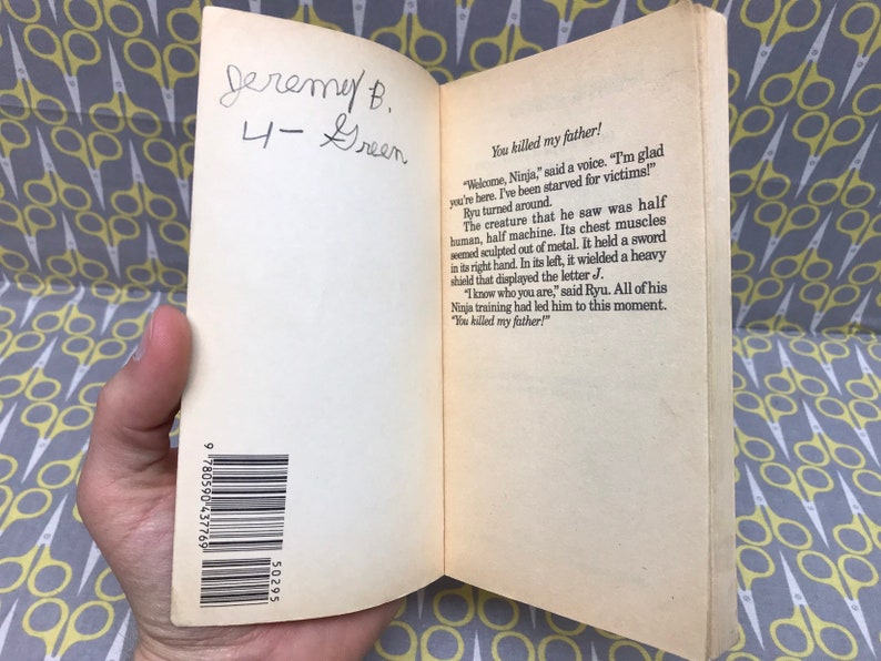 May include: A close-up of a book's back cover with a barcode and the text "You killed my father!"  The book is open to a page with text about a creature that is half human and half machine. The text also includes the name "Ryu".
