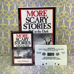 Puede incluir: Una colecci&oacute;n de casetes de audio antiguos y un libro titulado "More Scary Stories to Tell in the Dark". El libro y las cajas de casetes presentan el t&iacute;tulo en rojo y negro, con una ilustraci&oacute;n espeluznante. El casete es blanco.