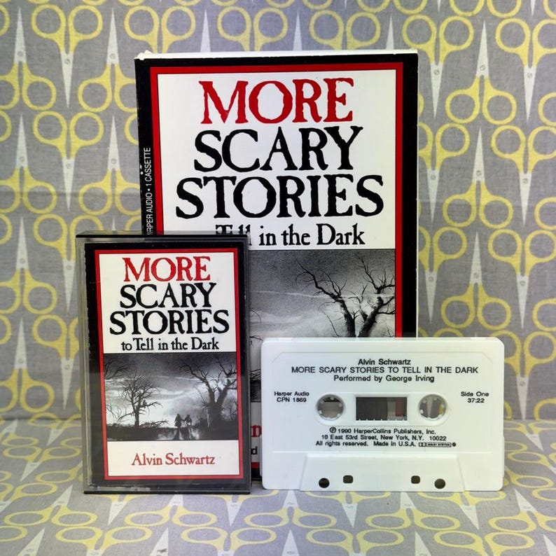Puede incluir: Una colecci&oacute;n de casetes de audio antiguos y un libro titulado "More Scary Stories to Tell in the Dark". El libro y las cajas de casetes presentan el t&iacute;tulo en rojo y negro, con una ilustraci&oacute;n espeluznante. El casete es blanco.