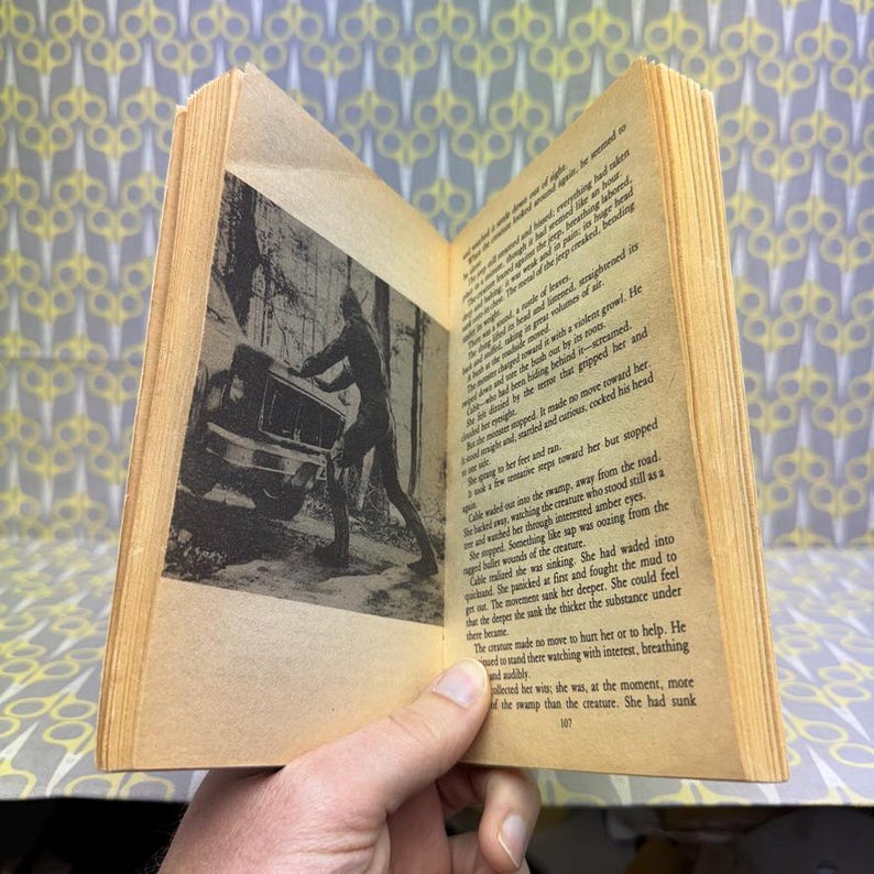 May include: An open vintage book with aged, yellowed pages. A black and white illustration depicts a person pushing a vehicle. The text on the pages is in English. The book is held open, revealing the text and illustration.