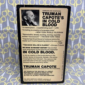 May include: A black and white book cover with a photo of Truman Capote. The title is "Truman Capote's In Cold Blood". The cover includes several quotes about the book, including "A masterpiece...a spellbinding work" and "No book in recent history has excited such enthusiasm as the spectacular bestseller In Cold Blood."
