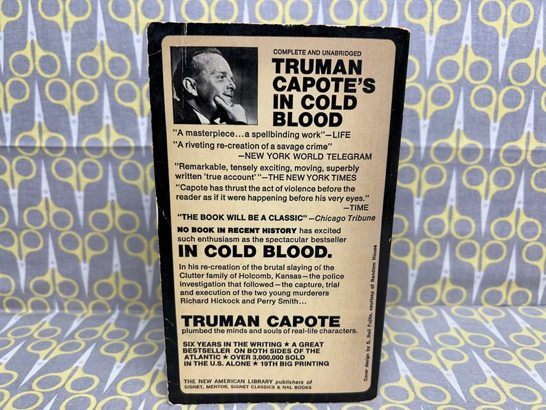 May include: A black and white book cover with a photo of Truman Capote. The title is "Truman Capote's In Cold Blood". The cover includes several quotes about the book, including "A masterpiece...a spellbinding work" and "No book in recent history has excited such enthusiasm as the spectacular bestseller In Cold Blood."