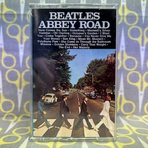 May include: A cassette tape case with a photo of the Beatles crossing Abbey Road. The case is clear plastic and the photo is a classic image of the band walking across the street.