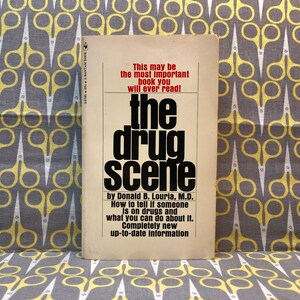 Può includere: Un libro tascabile vintage intitolato "The Drug Scene" di Donald B. Louria, M.D. La copertina è bianca con testo nero e rosso. Il libro tratta di come capire se qualcuno sta assumendo droghe e cosa puoi fare al riguardo.