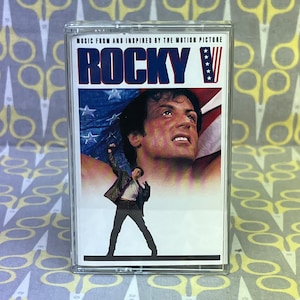 May include: A cassette tape with a picture of Sylvester Stallone on the cover. The tape is for the soundtrack of the movie "Rocky V".
