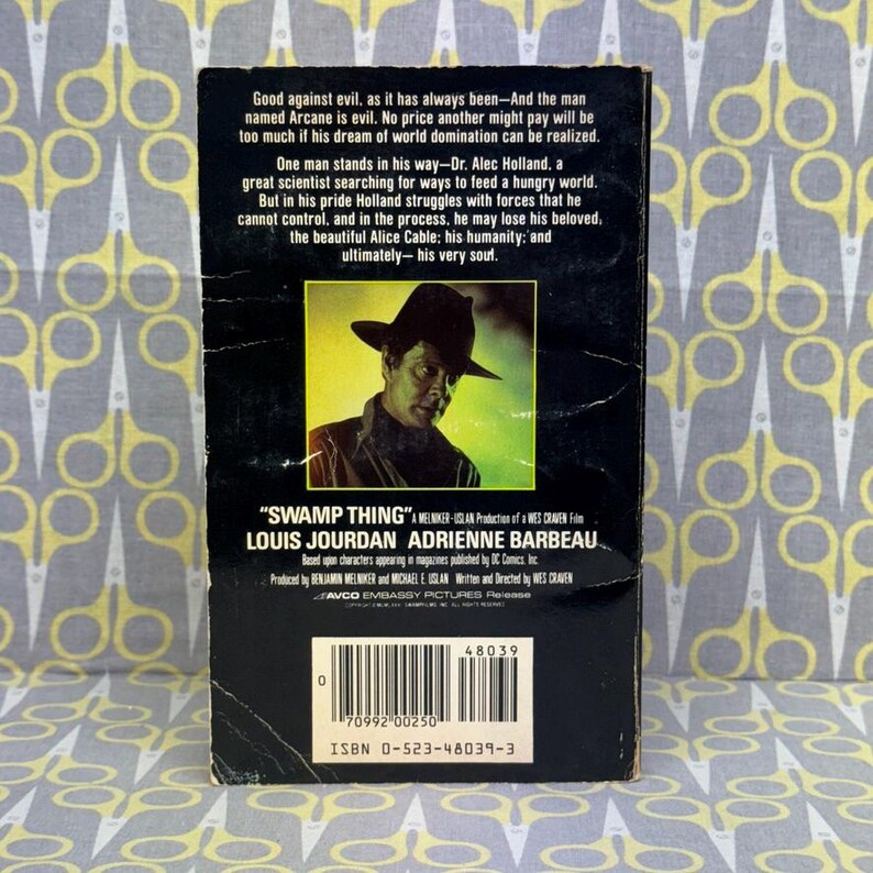 May include: A vintage paperback book with the title "Swamp Thing" and the names Louis Jourdan and Adrienne Barbeau. The cover features a man in a hat. The back cover has text about the story.