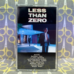 May include: A black cassette tape with a white label that reads "Less Than Zero". The image on the label is a man in a suit standing in front of a pool at night. The back of the cassette tape lists the artists featured on the compilation.
