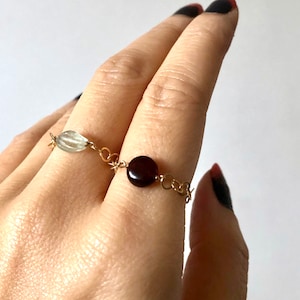 May include: A gold chain ring with a light green oval-shaped gemstone and a dark red round gemstone.
