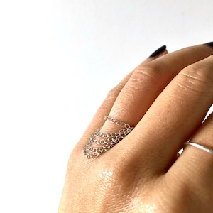 May include: A silver chain ring worn on a finger. The ring is made of multiple chains layered on top of each other.