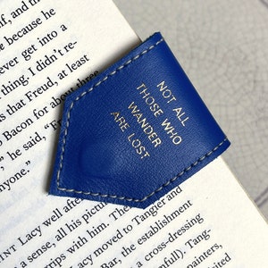 May include: A blue leather bookmark with a gold inscription that reads "Not all those who wander are lost."