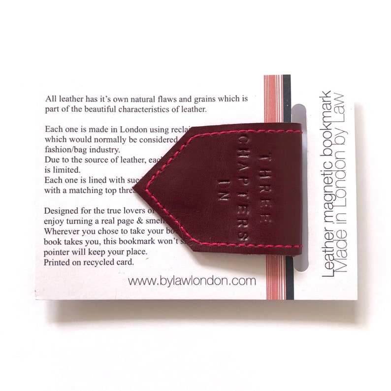 May include: A burgundy leather magnetic bookmark with pink stitching, featuring the text "THREE CHAPTERS IN." The bookmark is on a white card with text and the website bylawlondon.com.