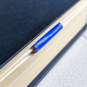May include: A black leather-bound book with a blue ribbon bookmark.