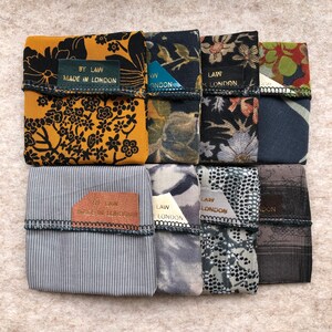 Pu&ograve; includere: Otto pochette in tessuto con diversi motivi e colori. Ogni pochette ha una piccola etichetta dorata con il testo "BY LAW MADE IN LONDON" o "LAW LONDON".