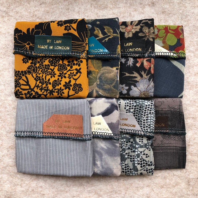 Pu&ograve; includere: Otto pochette in tessuto con diversi motivi e colori. Ogni pochette ha una piccola etichetta dorata con il testo "BY LAW MADE IN LONDON" o "LAW LONDON".