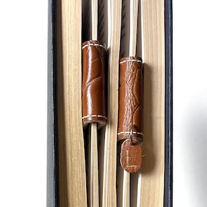 May include: Two brown leather bookmarks with a decorative pattern. The bookmark on the right has a silver charm with the letter "L" on it.