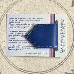 May include: A blue leather magnetic bookmark with white stitching. The bookmark is made in London by Law. The text on the card reads: "Designed for the true book lovers, worms and geeks, the ones who still enjoy turning a real page and smelling the paper. Wherever you chose to take your book or where book takes you, this bookmark won't slip, this pointer will keep your place. This bookmark is made in London, leather which would normally be used in the fashion/bag industry. Due to the source of leather, it is limited. Lined with either suede or organic leather, together with a matching top thread. All leather has it's own natural flaws and part of the beautiful characteristics of leather. Printed on recycled card. www.bylawlondon.com"