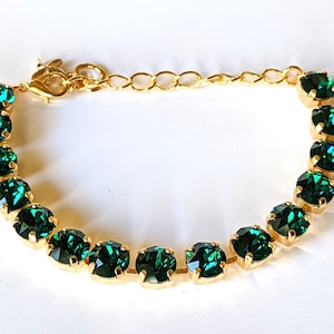 May include: A gold chain bracelet with a clasp closure and a row of emerald green crystal stones.