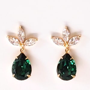 May include: A pair of gold earrings featuring a teardrop-shaped green gemstone and a cluster of clear stones in a flower design.