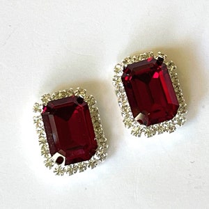 Peut inclure: Deux boucles d'oreilles en pierres précieuses rouges avec une bordure de strass argentés.