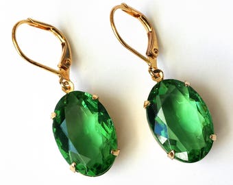 May include: A pair of gold earrings with large oval-shaped green gemstones. The earrings have a lever back closure.