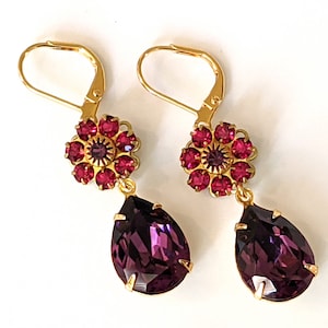 May include: Gold dangle earrings with a teardrop shaped purple crystal and a cluster of pink rhinestones in a flower shape.