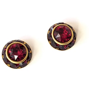 Peut inclure: Une paire de boucles d'oreilles en or avec un centre en strass rouge entouré de petits strass rouges.