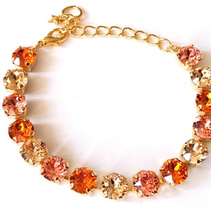 May include: A gold-toned bracelet featuring a series of round, orange and peach-colored crystals. The crystals are set in a gold metal band, with a lobster clasp closure and a small star charm. The bracelet is designed for a delicate and elegant look.