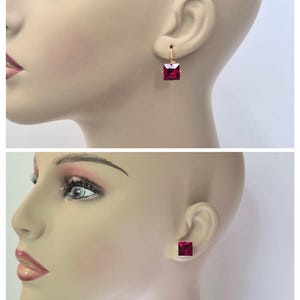May include: A pair of earrings and a stud earring are shown on a mannequin. The earrings are a deep red square gemstone set in gold-colored metal. One pair is a drop earring, and the other is a stud earring.
