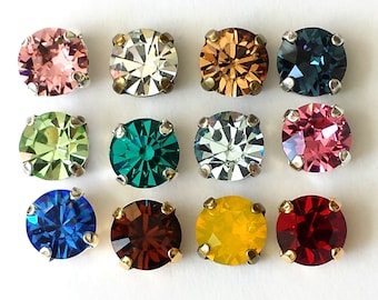 May include: Twelve round, faceted, glass rhinestones in various colors, including clear, green, blue, red, yellow, and pink. Each rhinestone is set in a silver-toned metal setting with four prongs.