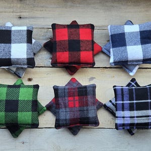 May include: Six square-shaped fabric bean bags in various plaid patterns. The bean bags are black and white, red and black, blue and white, green and black, gray and red, and purple and black.