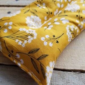 Puede incluir: Una almohada rectangular de tela amarilla con un patr&oacute;n floral blanco. La almohada es rectangular y tiene una costura en el medio.