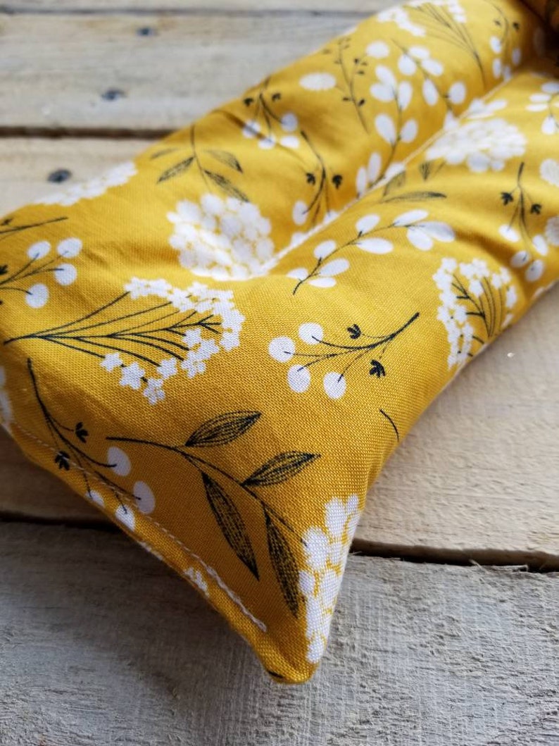 Puede incluir: Una almohada rectangular de tela amarilla con un patr&oacute;n floral blanco. La almohada es rectangular y tiene una costura en el medio.