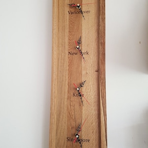 May include: A wooden wall clock with four clock faces, each displaying a different time zone. The time zones are Vancouver, New York, Korea, and Singapore. The clock is made of natural wood with a light brown finish.